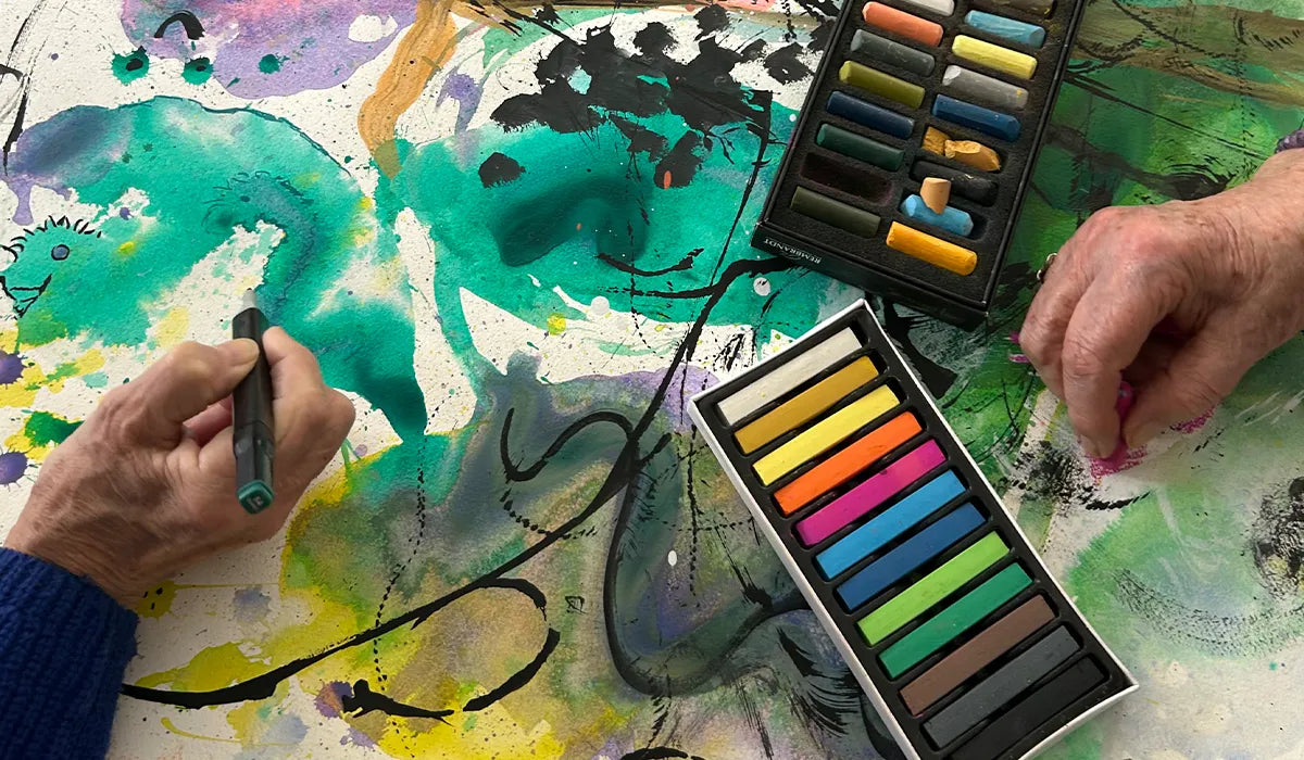 två äldre personer vars händer syns, de ritar med färgglada kritor på ett konstverk i gen-konst