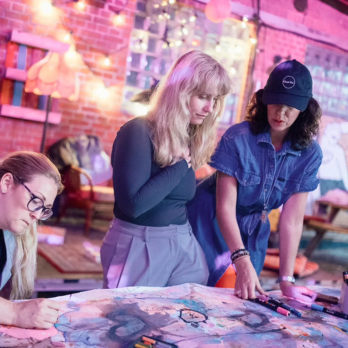 tre kvinnor lutar sig över ett stort konstverk som de skapat tillsammans